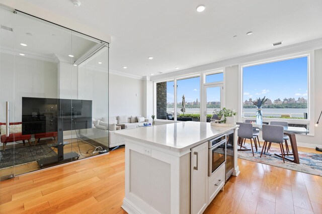 kitchen featuring ornamental molding, open floor plan, healthy amount of natural light, white cabinets, and light wood finished floors