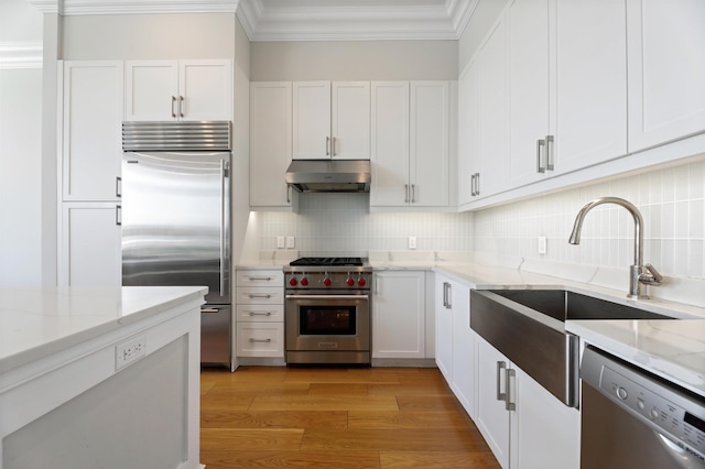 kitchen with high quality appliances, under cabinet range hood, crown molding, a sink, and white cabinetry