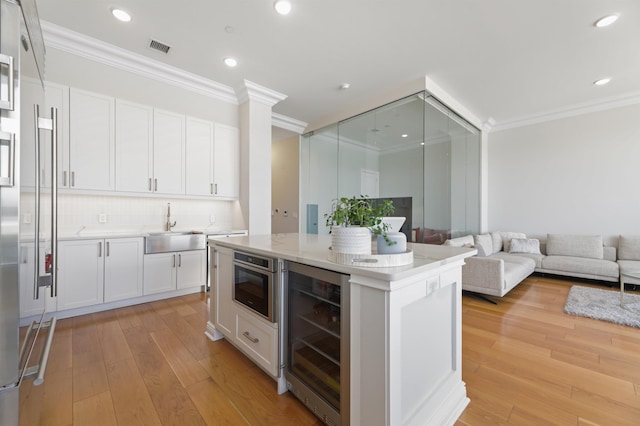 kitchen with beverage cooler, a sink, crown molding, light wood-type flooring, and white cabinetry