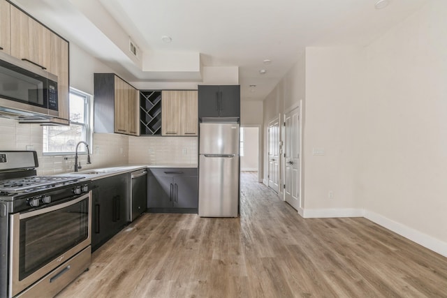 kitchen with sink, light brown cabinets, stainless steel appliances, backsplash, and hardwood / wood-style floors