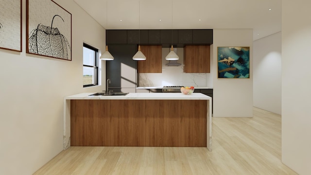 kitchen with wall chimney exhaust hood, sink, tasteful backsplash, light wood-type flooring, and decorative light fixtures