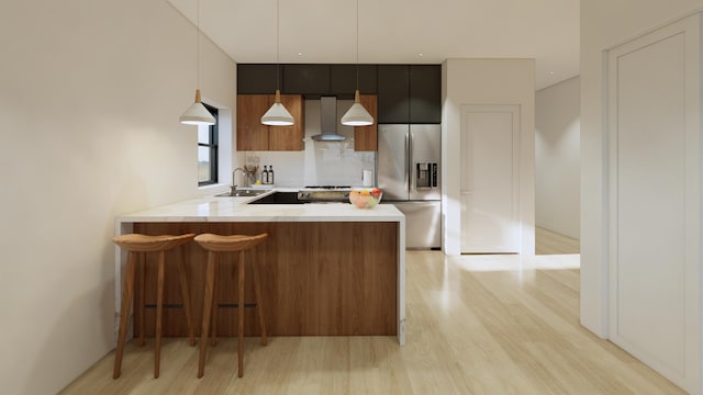 kitchen featuring kitchen peninsula, hanging light fixtures, stainless steel fridge with ice dispenser, wall chimney range hood, and light hardwood / wood-style flooring