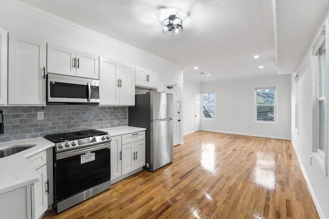 kitchen with white cabinetry, appliances with stainless steel finishes, tasteful backsplash, light hardwood / wood-style flooring, and sink