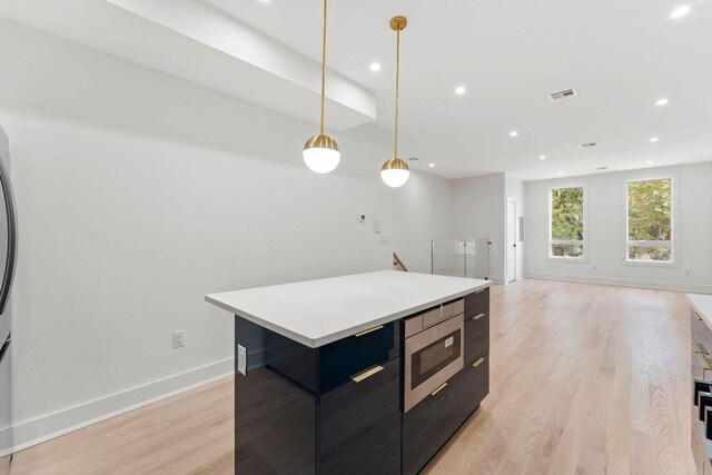 kitchen with modern cabinets, a kitchen island, stainless steel microwave, light countertops, and pendant lighting