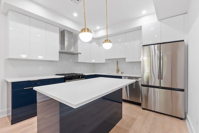 kitchen with a center island, wall chimney range hood, hanging light fixtures, white cabinetry, and stainless steel appliances