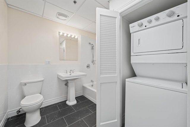 300 Communipaw Ave Unit 122, Jersey City, NJ 07304 - full bathroom with stacked washing machine and dryer, tile patterned floors, tile walls, wainscoting, and shower / bathtub combination