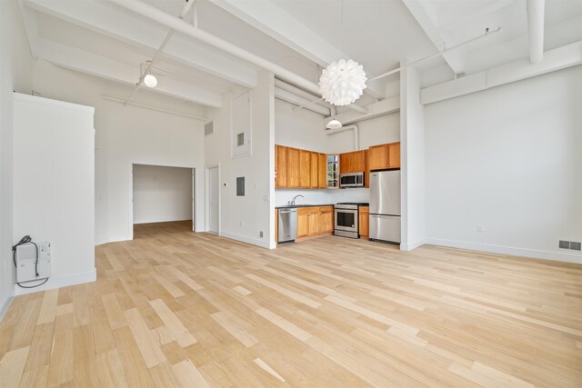 300 Communipaw Ave Unit 122, Jersey City, NJ 07304 - kitchen featuring appliances with stainless steel finishes, a high ceiling, brown cabinetry, light wood finished floors, and hanging light fixtures