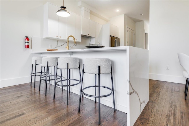 kitchen featuring a breakfast bar, light countertops, freestanding refrigerator, white cabinetry, and dark wood-style flooring