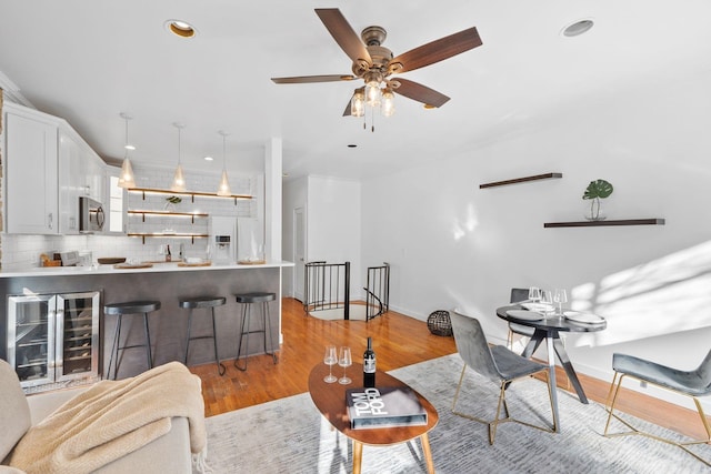 living area featuring baseboards, a ceiling fan, wine cooler, recessed lighting, and light wood-style flooring
