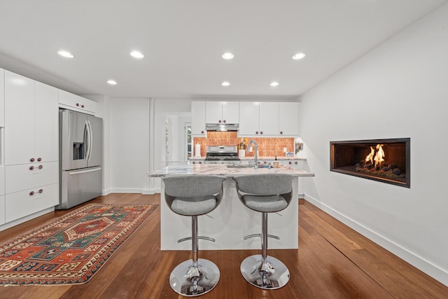 kitchen with sink, white cabinetry, a kitchen island with sink, stainless steel appliances, and a kitchen bar