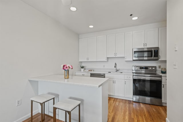 kitchen featuring stainless steel appliances, a breakfast bar, white cabinetry, and a sink