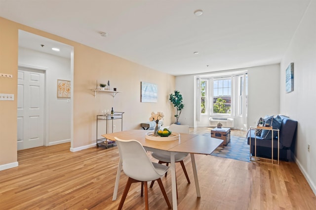 dining space with an AC wall unit, baseboards, and light wood-style floors