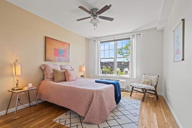 bedroom with baseboards, a ceiling fan, light wood finished floors, and a wall mounted AC