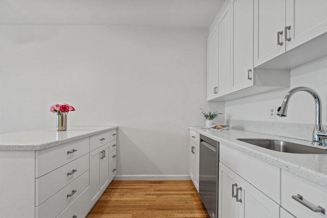kitchen with a sink, light wood finished floors, dishwasher, white cabinetry, and baseboards