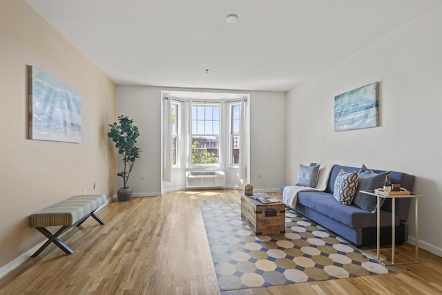 sitting room with baseboards, a wall unit AC, and light wood-style floors