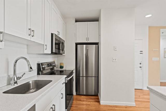 kitchen with a sink, white cabinets, stainless steel appliances, and light wood-type flooring