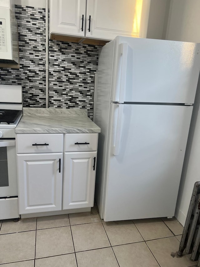 kitchen with decorative backsplash, light tile patterned floors, white cabinets, and white appliances