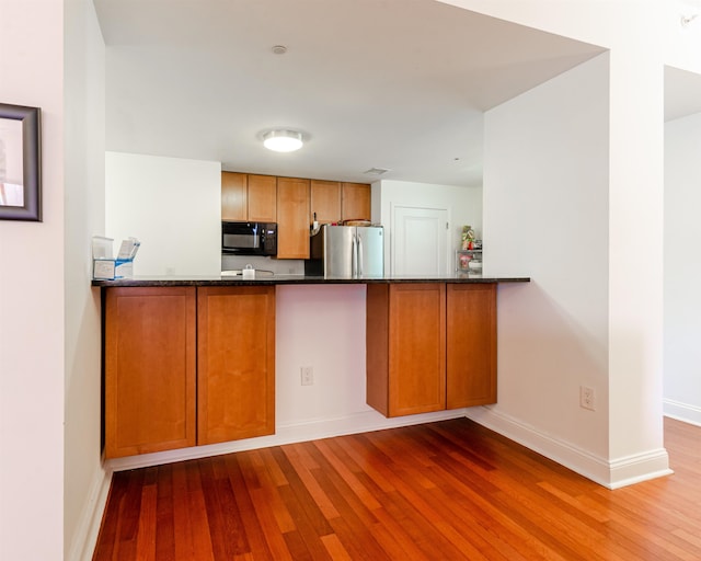 kitchen with kitchen peninsula, wood-type flooring, dark stone countertops, and stainless steel refrigerator