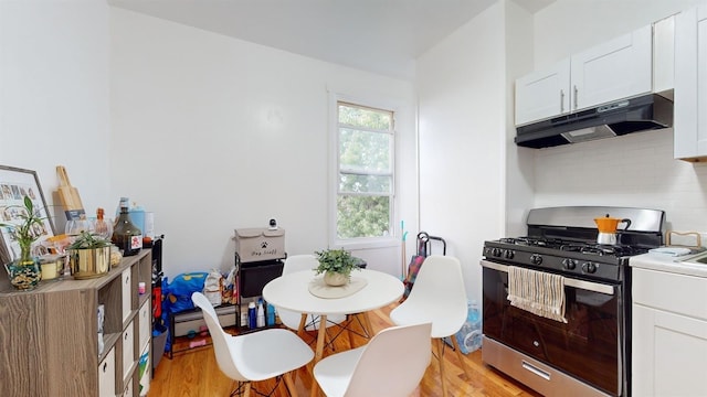 kitchen with tasteful backsplash, white cabinets, light wood-type flooring, under cabinet range hood, and stainless steel gas range oven
