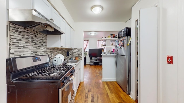 kitchen with tasteful backsplash, white cabinetry, under cabinet range hood, light wood-style floors, and appliances with stainless steel finishes