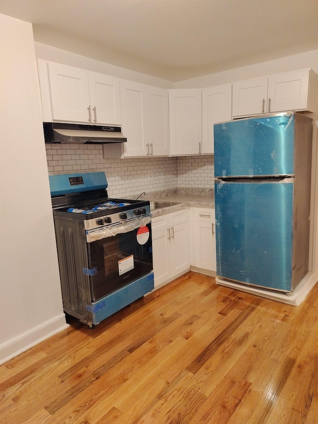 kitchen featuring white cabinets, freestanding refrigerator, under cabinet range hood, light wood finished floors, and stainless steel gas range oven