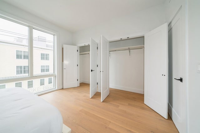 bedroom featuring multiple closets, light wood-style flooring, and baseboards