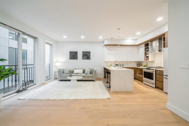 kitchen with open shelves, gas range, wall chimney exhaust hood, a sink, and open floor plan