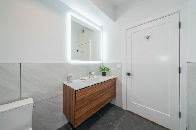 bathroom featuring toilet, tile patterned floors, vanity, and tile walls