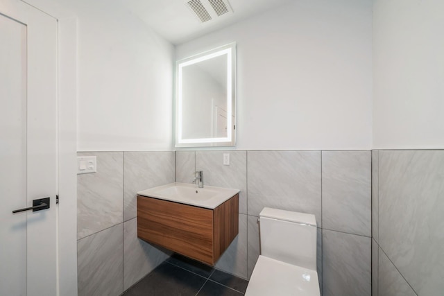 half bath with toilet, tile walls, vanity, visible vents, and tile patterned floors