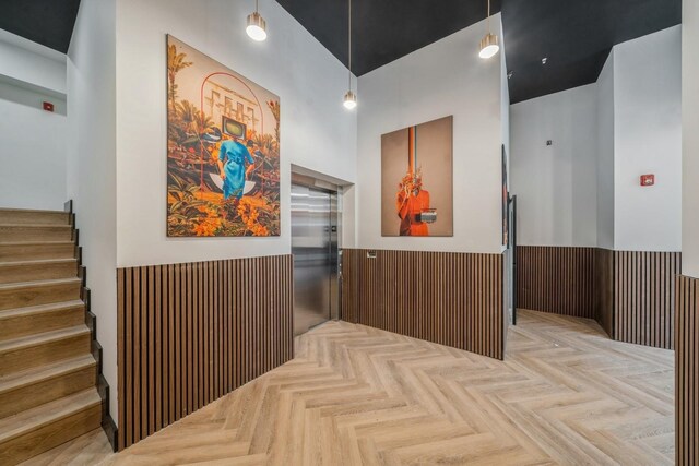 hall featuring stairway, wainscoting, elevator, and wooden walls