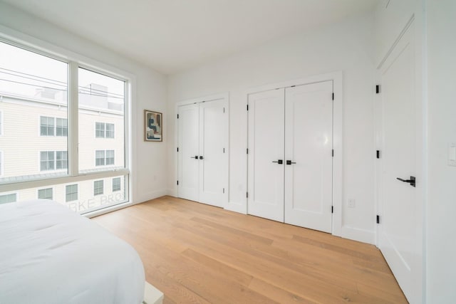 bedroom with light wood-style floors, baseboards, and two closets