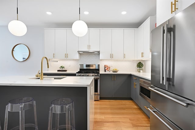 77 Clerk St Unit 1, Jersey City, NJ 07305 - kitchen with under cabinet range hood, a sink, a kitchen bar, hanging light fixtures, and appliances with stainless steel finishes