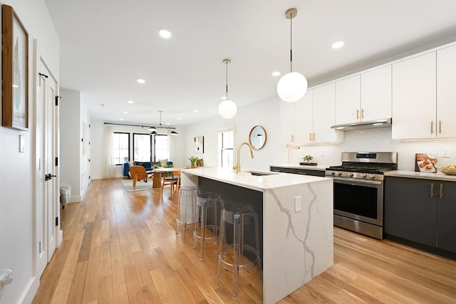 77 Clerk St Unit 1, Jersey City, NJ 07305 - kitchen featuring under cabinet range hood, stainless steel gas range oven, a breakfast bar, a sink, and decorative backsplash