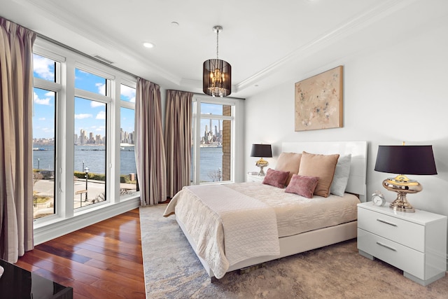 bedroom featuring hardwood / wood-style floors, ornamental molding, a raised ceiling, a water view, and an inviting chandelier