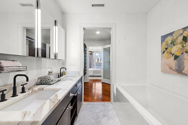 bathroom featuring tile walls, vanity, and tiled tub