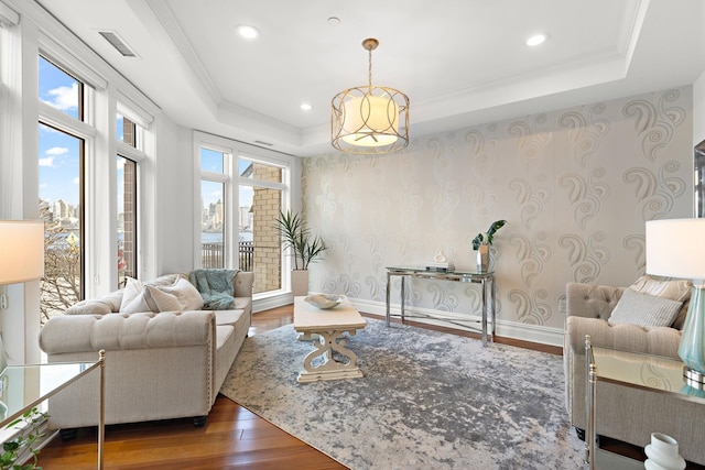 living room with a raised ceiling, ornamental molding, dark wood-type flooring, and a wealth of natural light