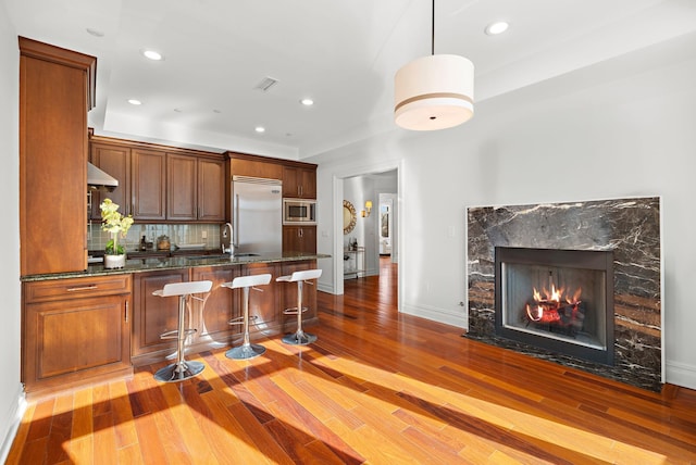 kitchen featuring a breakfast bar, decorative light fixtures, sink, decorative backsplash, and built in appliances