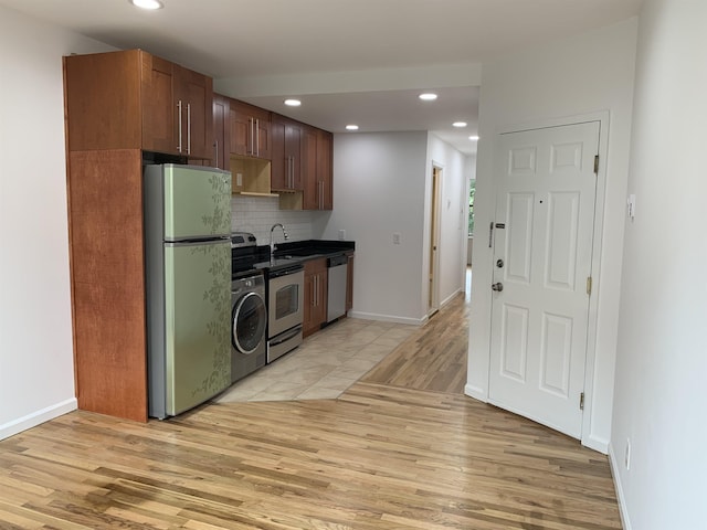 kitchen with appliances with stainless steel finishes, light wood-type flooring, backsplash, washer / clothes dryer, and dark countertops