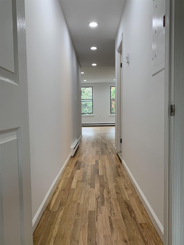 corridor featuring a baseboard heating unit, light wood-type flooring, and baseboards