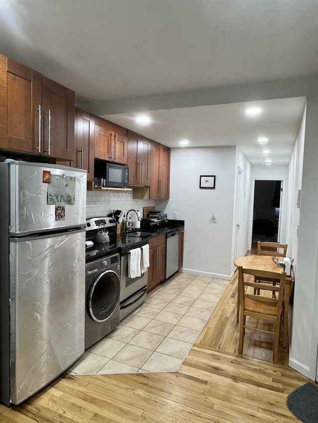 kitchen featuring stainless steel appliances, light wood-type flooring, backsplash, dark countertops, and washer / dryer