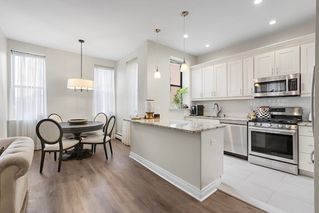 kitchen featuring a sink, light stone counters, appliances with stainless steel finishes, white cabinets, and decorative backsplash