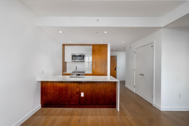 kitchen featuring kitchen peninsula, decorative backsplash, light wood-type flooring, and white cabinetry