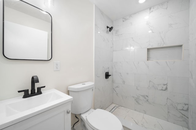 bathroom featuring vanity, a tile shower, and toilet