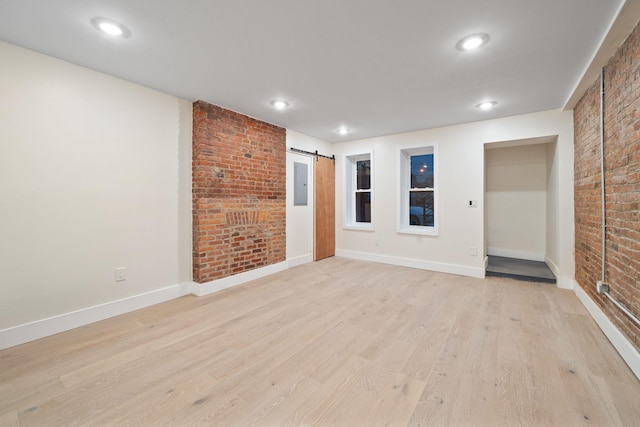 unfurnished room with brick wall, a barn door, electric panel, and light hardwood / wood-style flooring