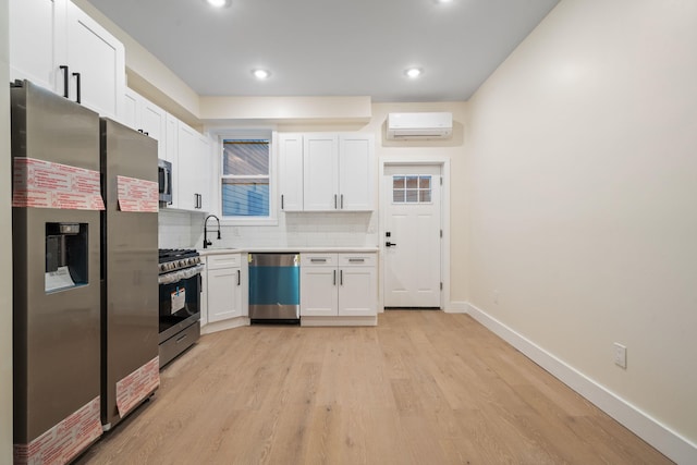 kitchen featuring appliances with stainless steel finishes, white cabinetry, decorative backsplash, a wall unit AC, and light hardwood / wood-style flooring