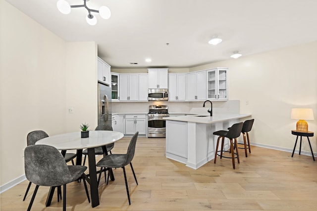 kitchen featuring appliances with stainless steel finishes, light wood-type flooring, kitchen peninsula, white cabinets, and sink