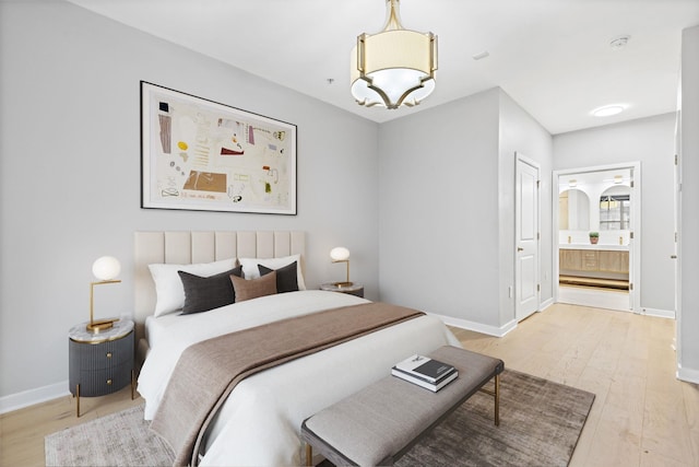 bedroom with ensuite bathroom, an inviting chandelier, and light wood-type flooring