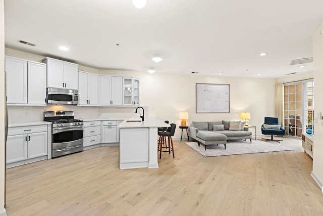 kitchen with white cabinetry, a kitchen breakfast bar, light hardwood / wood-style flooring, an island with sink, and appliances with stainless steel finishes