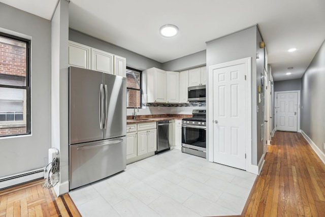 kitchen with stainless steel appliances, white cabinets, decorative backsplash, sink, and light hardwood / wood-style flooring