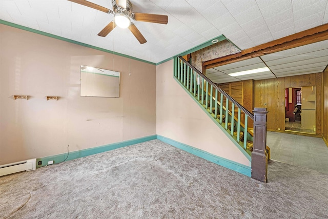 spare room featuring a ceiling fan, carpet flooring, wooden walls, and stairs